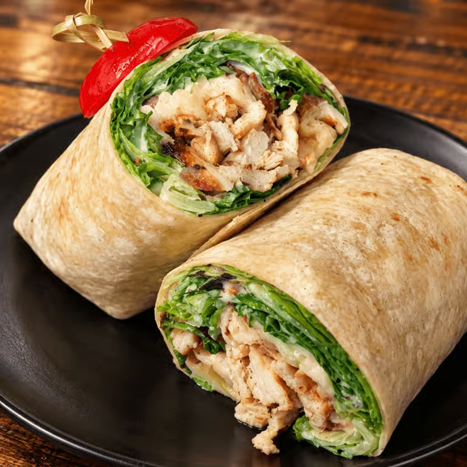 Two grilled chicken wraps filled with lettuce and vegetables, served on a black plate over a rustic wooden table.